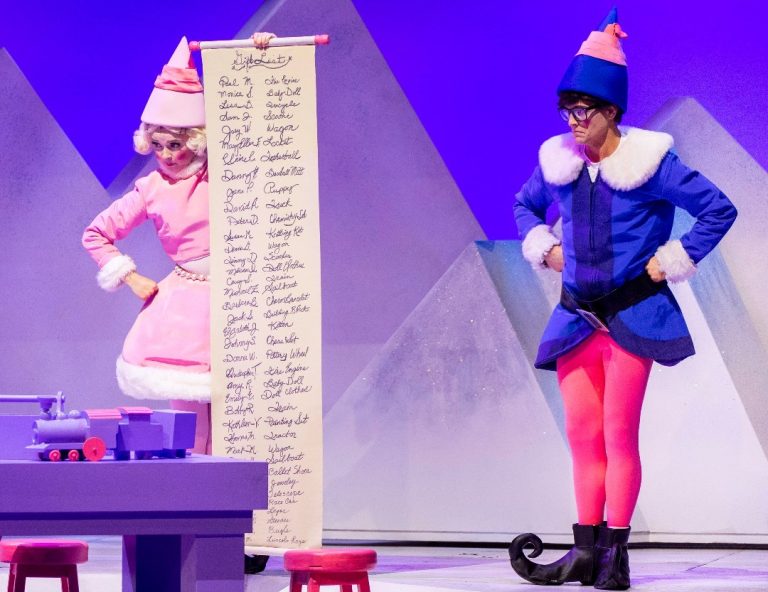 Two people dressed up as elves on stage with a long Christmas list.